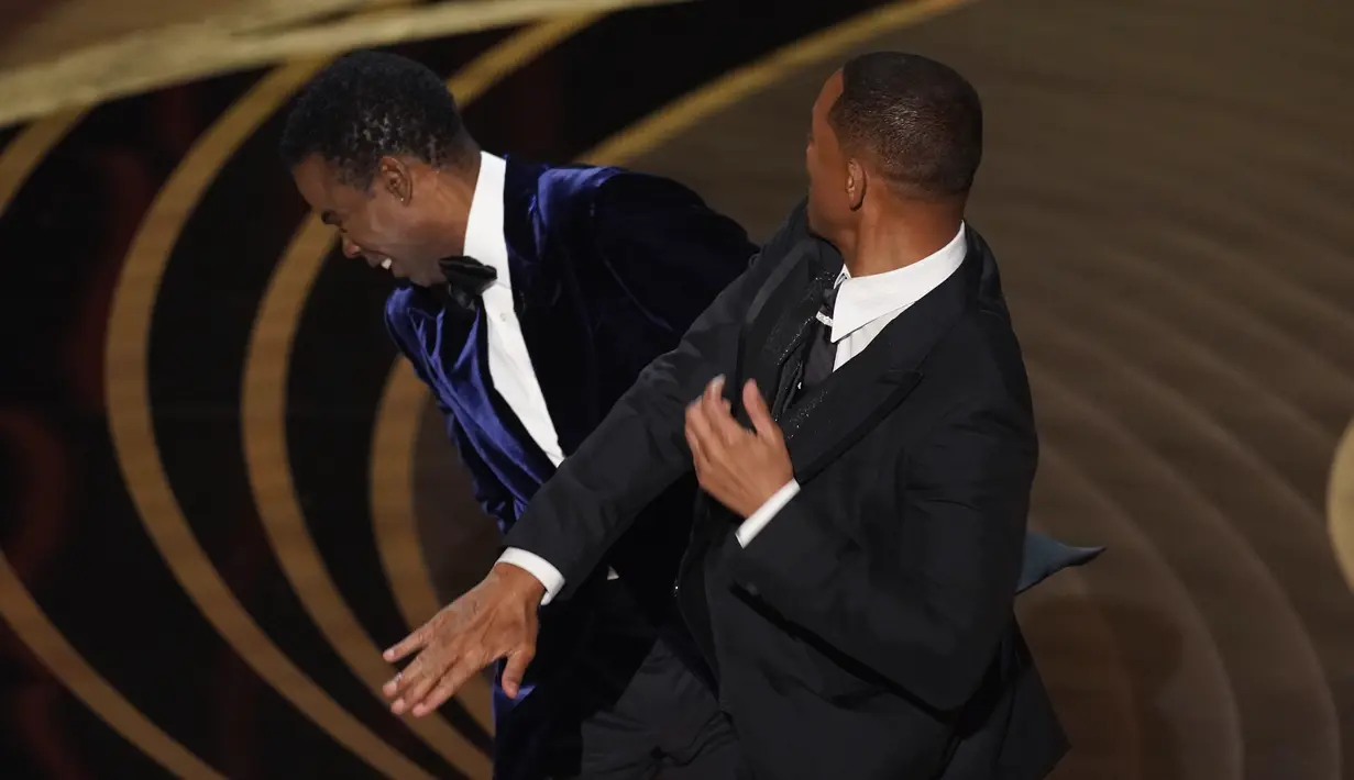 Will Smith (kanan) memukul presenter Chris Rock di atas panggung Piala Oscar 2022 saat mempersembahkan penghargaan untuk film dokumenter terbaik di Dolby Theatre, Minggu (27/3/2022). Will Smith merasa lawakan sang komedian terkait istrinya, Jada Pinkett Smith keterlaluan. (AP Photo/Chris Pizzello)