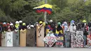 Pengunjuk rasa berdiri dengan perisai sambil mengibarkan bendera Kolombia di sekitar barikade yang terbakar selama protes anti-pemerintah di Bogota (28/5/2021). Warga Kolombia telah turun ke jalan selama berminggu-minggu setelah pemerintah mengusulkan kenaikan pajak. (AP Photo/Ivan Valencia)