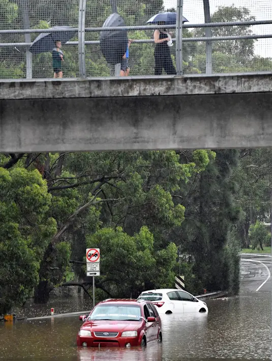 Warga menggunakan jembatan penyeberangan saat air banjir mencapai daerah pemukiman di pinggiran barat daya Sydney, Australia, Selasa (8/3/2022). Ribuan warga Sydney diminta untuk mengungsi dari daerah dataran rendah karena hujan lebat dan banjir bandang. (Muhammad FAROOQ/AFP)