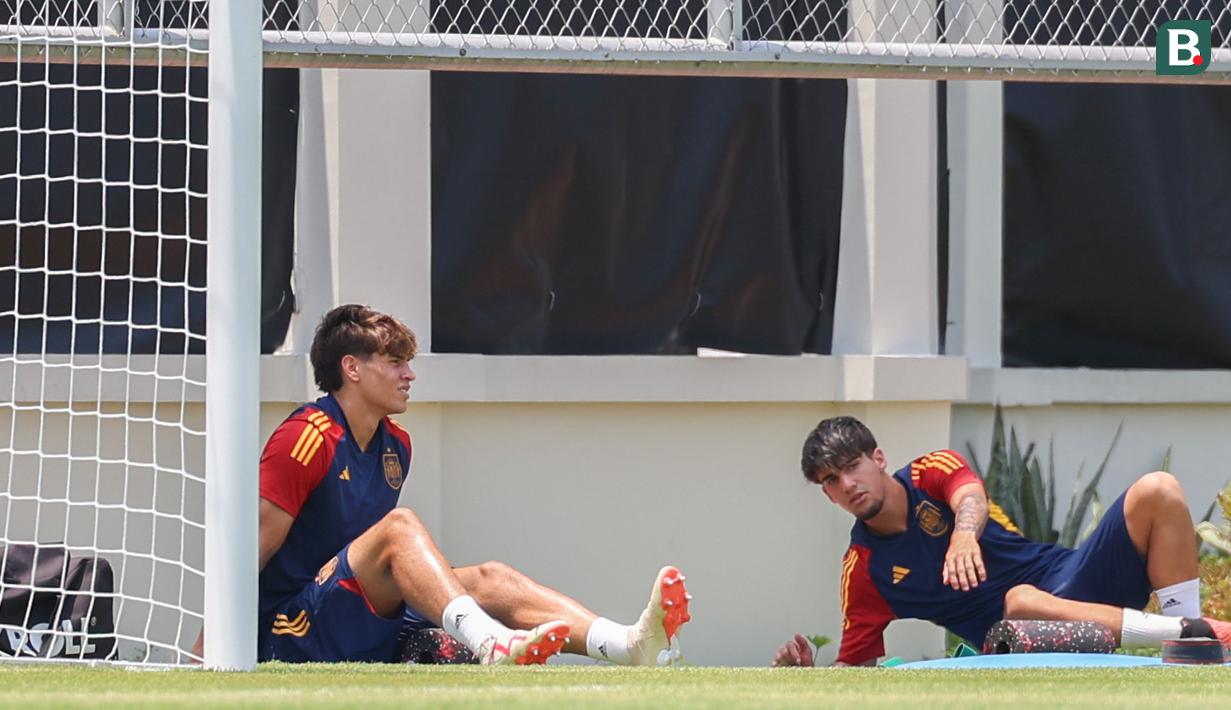 Pemain Timnas Spanyol U-17, Marc Guiu (kiri), mencari tempat teduh saat menjalani latihan dibawah sinar terik matahari yang berlangsung di Lapangan Sriwaru, Kecamatan Laweyan, Kota Solo, Rabu (8/11/2023). (Bola.com/Radifa Arsa)