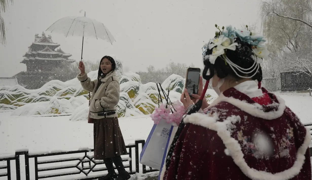 Seorang wanita berpose untuk foto di dekat Kota Terlarang saat salju turun di Beijing, China (18/3/2022). Sebagian besar distrik di ibu kota China, Beijing, mengalami salju pada hari Kamis, dengan distrik paling utara Yanqing melaporkan hujan salju terberat. (AP Photo/Ng Han Guan)
