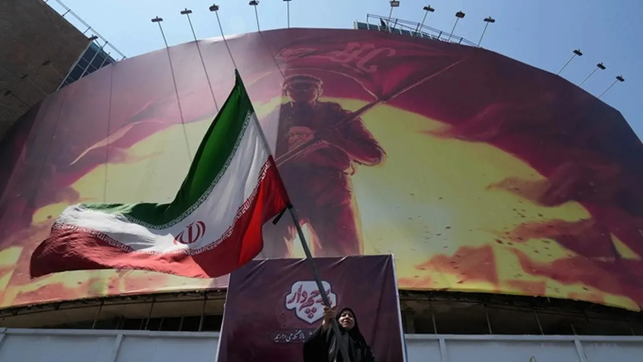 Seorang perempuan mengibarkan bendera Iran di dekat papan reklame bergambar mendiang Pemimpin Tertinggi Iran Ayatollah Ali Khamenei di pusat kota Teheran, Iran, Sabtu (1/8/2026).