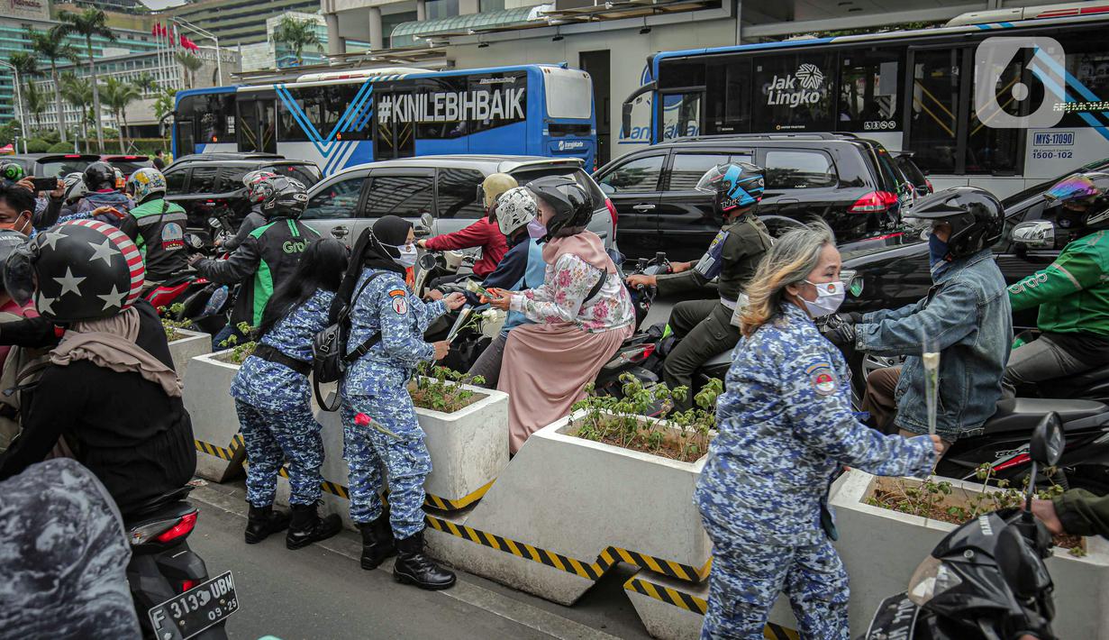 Sejumlah perserta yang tergabung dalam Forum Kader Bela Negara DKI Jakarta membagikan bunga dan masker kepada pengguna jalan di Jalan Thamrin, Jakarta, Rabu (22/12/2021). Aksi tersebut merupakan bentuk apresiasi terhadap kaum perempuan terutama pada peringatan Hari Ibu. (Liputan6.com/Faizal Fanani)