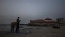 Dua warga Palestina melaksanakan sholat saat yang lain berbuka puasa di hari Ramadhan di pantai di Kota Gaza (2/5/2021).  Setelah peningkatan tajam kasus COVID-19 di Gaza, Hamas kembali memperketat pembatasan atas desakan pejabat kesehatan. (AP Photo/Khalil Hamra)