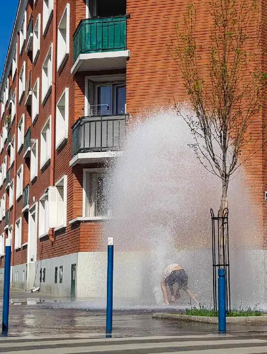 Seorang pria mendinginkan tubuh di dalam air hidran yang terbuka selama cuaca panas di Aubervilliers, sebelah utara Paris, (19/4). (AFP Photo/Amine Guedaim)