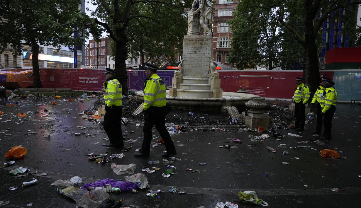 Petugas polisi berdiri di antara sampah yang ditinggalkan penggemar Skotlandia yang berpesta sebelum pertandingan grup D antara Inggris melawan Skotlandia di dekat patung William Shakespeare di Leicester Square di London, Jumat (18/6/2021). (AP Photo/Kirsty Wigglesworth)
