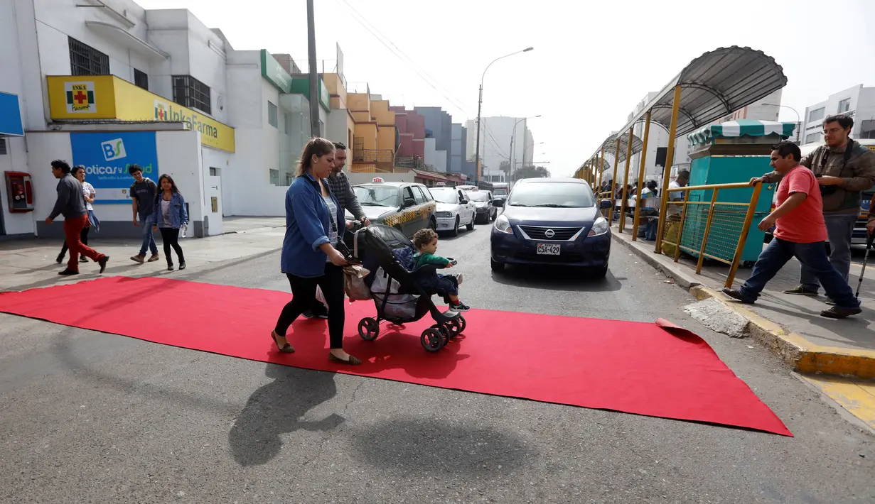 Warm berjalan di atas karpet merah yang terbentang di salah satu ruas jalan di distrik Magdalena del Mar, Lima, Peru, (2/7). Aksi ini dilakukan untuk menggugah kesadaran warga perkotaan agar menghormati pejalan kaki. (REUTERS / Guadalupe Pardo)