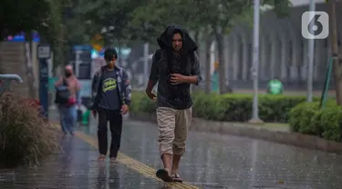 Warga menutupi kepala dari guyuran hujan saat melintasi kawasan Sudirman, Jakarta, Kamis (4/1/2024). (Liputan6.com/Angga Yuniar)