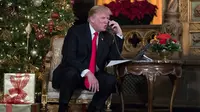 Presiden Donald Trump berbicara dengan anak-anak di telepon saat mereka mengiktui NORAD Tracks Santa di Palm Beach, AS (24/12). Acara NORAD Tracks Santa ini mengandalkan sukarelawan untuk menerima telepon dari anak-anak. (AP Photo/Carolyn Kaster)
