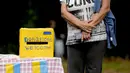 Seorang perempuan menunggu di dekat kotak sumbangan pada perayaan Hari Kemerdekaan Ukraina di sebuah perayaan di Chichester, Inggris selatan, Sabtu, 27 Agustus 2022. Chichester dinobatkan sebagai daerah paling dermawan di negara itu untuk menampung pengungsi Ukraina. (AP Photo/Frank Augstein)