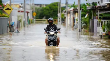 Seorang pria mengendarai sepeda motornya menerjang banjir di Batu Berendam, Malaka, Malaysia, 3 Januari 2022. Banjir besar masih terus menerjang negeri jiran Malaysia. (NAZRULHAD HASHIM/AFP)