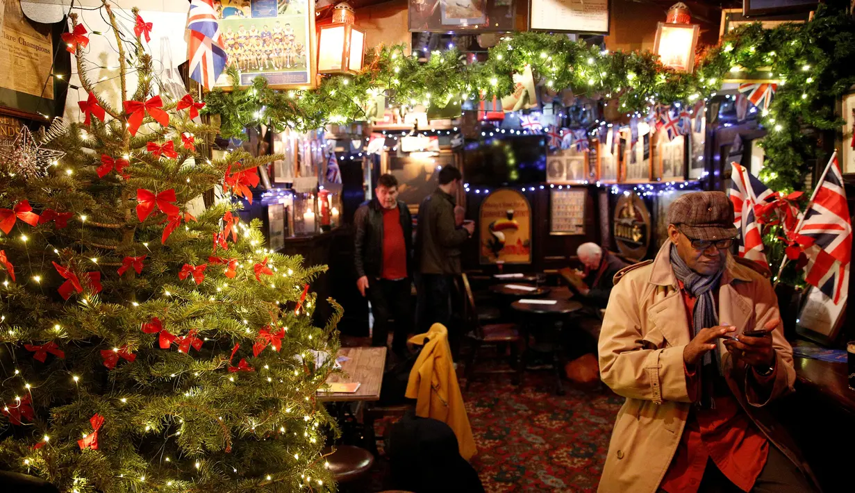 Seorang pelanggan menikmati dekorasi natal di bar The Churchill Arms di London, Inggris, 20 Desember 2016. Menyambut Natal, bagian luar bangunan bar tersebut ditutupi lebih dari 80 pohon natal dan hampir 22.000 lampu berkelap-kelip. (REUTERS/Neil Hall)
