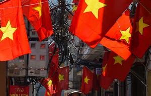 Seorang wanita mengendarai sepeda di sepanjang gang yang didekorasi dengan bendera nasional Vietnam menjelang perayaan Hari Nasional Vietnam di Hanoi (1/9/2020). Peringatan 75 tahun Hari Nasional Vietnam jatuh pada tanggal 2 September 2020. (AFP Photo/Nhac Nguyen)