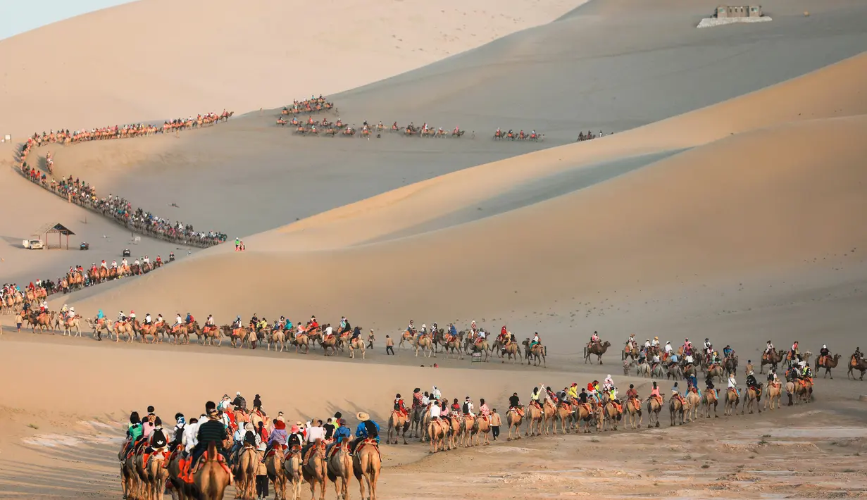 Para wisatawan menaiki unta di padang pasir di Dunhuang di provinsi Gansu di China barat laut (10/8/2019). Dunhuang adalah sebuah kota tingkat kabupaten di barat laut provinsi Gansu, Tiongkok Barat. (AFP Photo/Str)