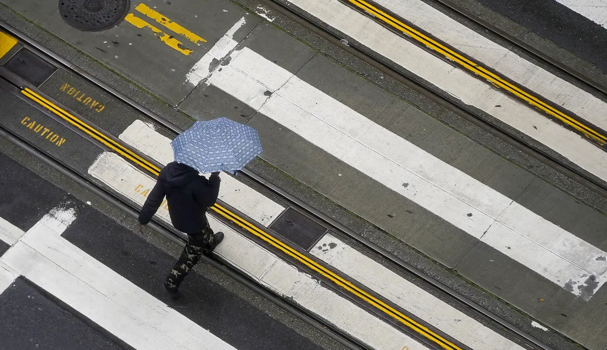 Pejalan kaki menyeberang jalan di San Francisco, Senin (13/12/2021). Badai musim dingin besar yang melanda California Utara diperkirakan akan meningkat dan perjalanan transportasi tertunda serta ancaman banjir lokal setelah musim gugur yang tidak normal di AS Barat. (AP Photo/Jeff Chiu)