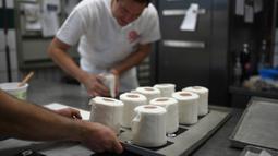 Pemilik toko roti Tim Kortuem menyiapkan kue berbentuk tisu toilet di toko roti Schuerener Backparadies di Dortmund, Jerman, 26 Maret 2020. Kelangkaan kertas tisu toilet memunculkan ide bagi pemilik toko roti itu membuat kue menyerupai barang yang diburu warga di tengah Covid-19 (Ina FASSBENDER/AFP)