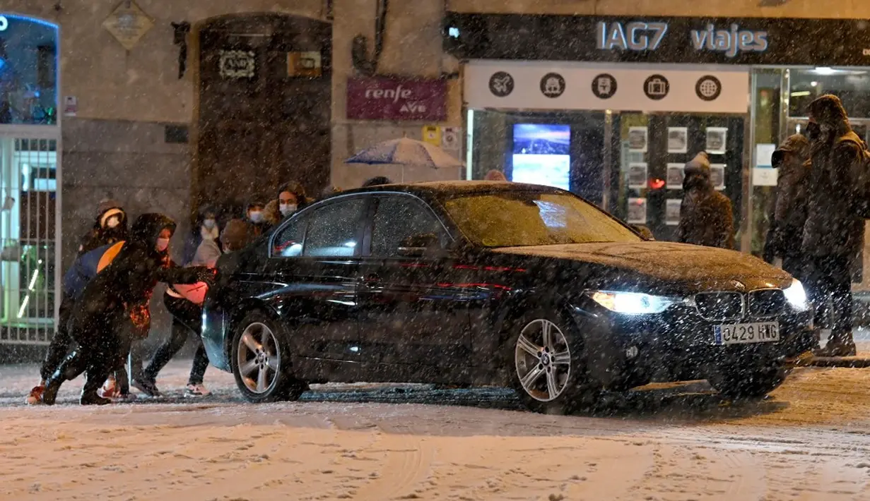 Warga mendorong mobil yang terjebak salju tebal di Madrid, Spanyol, Jumat (8/1/2021). Ribuan mobil terjebak salju tebal akibat Badai Filomena yang menghantam Madrid dan sebagian besar wilayah Spanyol. (OSCAR DEL POZO/AFP)