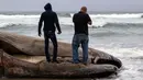 Dua orang berdiri di atas bangkai ikan paus yang terdampar di sebuah pantai kawasan Rosarito, Meksiko, Senin (22/5). Bangkai paus abu-abu itu diduga terbawa gelombang besar air laut hingga terbawa ke bibir pantai RosarIto. (AFP PHOTO/GUILLERMO ARIAS)