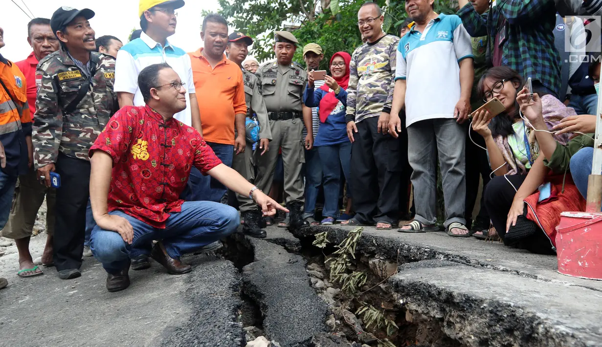 Gubernur DKI Anies Baswesdan berjongkok memeriksa retakan jalan di Kelurahan Kebon Manggis, Kecamatan Matraman, Jakarta Timur, Jumat (16/2). Kehadiran Anies yang mengenakan baju tradisional China itu mengundang perhatian warga. (Liputan6.com/Johan Tallo)