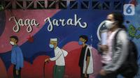 Warga yang mengenakan masker berjalan melintasi mural berisi imbauan terkait COVID-19 di Menteng, Jakarta, Kamis (7/10/2021). Pemerintah menyiapkan langkah implementasi prokes 3M, implementasi surveilans 3T, percepatan vaksinasi dan persiapan fasilitas rumah sakit. (Liputan6.com/Johan Tallo)