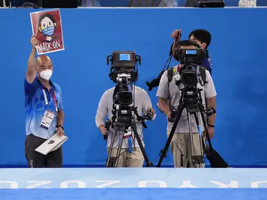 Manajer foto senam gymnastics, Rich Lam mengangkat tanda yang memberi isyarat kepada para atlet untuk mengenakan masker mereka saat seremoni penyerahan medali cabang senam nomor artistik putra Olimpiade Tokyo 2020 di Tokyo, Senin (26/7/2021). (AP Photo/Ashley Landis)