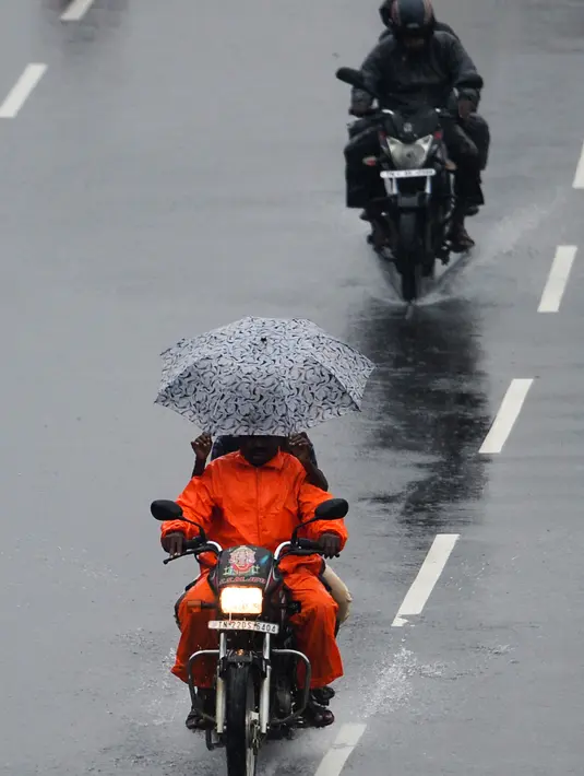 Pengendara sepeda motor menggunakan payung berkendara di sepanjang jalan di bawah hujan lebat di Chennai ketika topan Nivar mendekati pantai tenggara negara itu, (25/11/2020). (AFP/Arun Sankar)