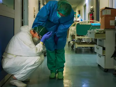 Seorang perawat dengan alat pelindung diri menghibur rekannya saat berganti shift di rumah sakit Cremona, tenggara Milan, Lombardy pada 13 Maret 2020. Jumlah kematian akibat Covid-19 di Italia sekarang yang tertinggi di dunia, menyalip China tempat wabah ini pertama kali. (Paolo MIRANDA/AFP)