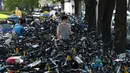 Seorang pria berjalan melintasi sepeda-sepeda yang diparkir memenuhi trotoar di Beijing, China (21/7/2020). Selama dua tahun terakhir, Pemerintah Beijing telah menyediakan fasilitas persewaan sepeda menggunakan sistem bike sharing. (AFP Photo/Greg Baker)