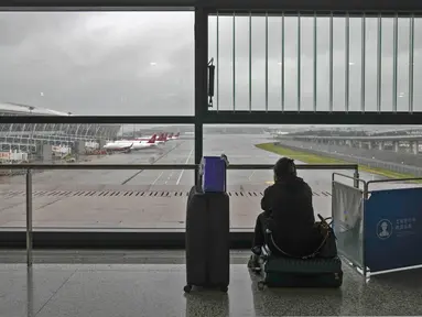 Seorang calon penumpang duduk di kopernya mengamati pesawat yang diparkir di landasan setelah semua penerbangan dibatalkan di Bandara Internasional Pudong, Shanghai, Minggu (25/7/2021). Ratusan jadwal penerbangan dibatalkan saat topan In-Fa bergerak menuju mendarat. (AP Photo/Andy Wong)