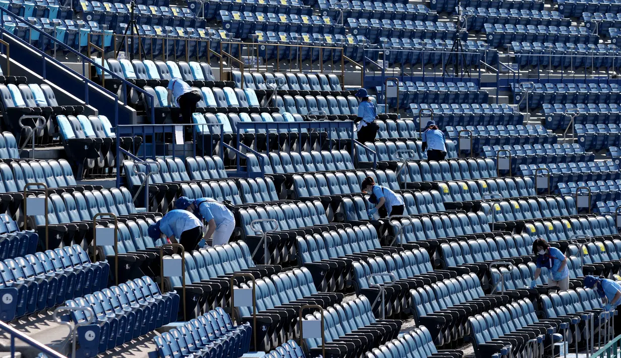 Relawan mendisinfektan kursi setelah pertandingan perebutan medali perunggu softball Olimpiade Tokyo 2020 antara Meksiko dan Kanada di Stadion Baseball Yokohama, pada 27 Juli 2021. Olimpiade yang digelar saat pandemi COVID-19 tersebut menerapkan protokol kesehatan ketat. (KAZUHIRO FUJIHARA / AFP)