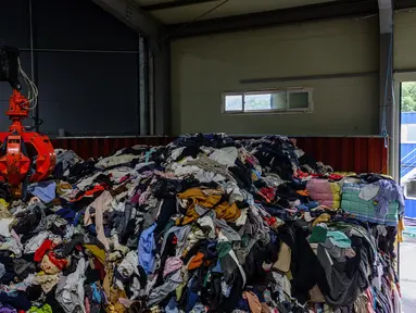 Dalam foto yang diambil pada tanggal 7 Agustus 2024 memperlihatkan seorang karyawan berjalan melewati gudang yang berisi tumpukan besar garmen, tempat tidur, mainan lunak, dan aksesori yang dikategorikan dengan cakar mekanis, sebelum diekspor ke luar negeri, di pabrik pakaian bekas di Paju, sekitar 28 km sebelah utara Seoul, Korea Selatan. (ANTHONY WALLACE/AFP)
