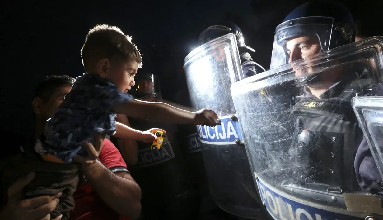 Seorang anak imigran di depan polisi Slovenia yang menghadang mereka di Harmica, Kroasia (18/9/2015). (REUTERS / Srdjan Zivulovic)