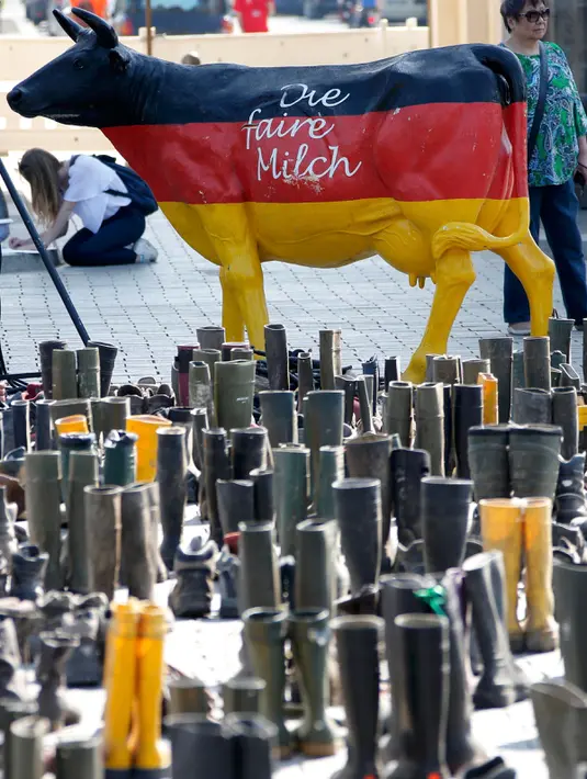 Patung sapi dan ratusan pasang sepatu boots diletakkan di depan gerbang Brandenburg, Berlin, Jerman, Senin (30/5).  Aksi protes oleh peternak sapi perah itu untuk menuntut harga produk susu yang lebih adil. (REUTERS/Fabrizio Bensch)