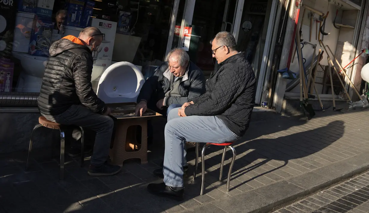 Orang-orang duduk dan bermain backgammon di depan sebuah toko di pasar di distrik Fatih Istanbul, Turki, Selasa, 3 Januari 2023. Menurut data resmi, harga konsumen naik 1,2% di Desember secara bulanan, dibandingkan dengan 2,9% pada November. (AP Photo/Khalil Hamra)