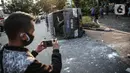 Seorang pria mengambil gambar sebuah mobil polisi yang dirusak massa saat bentrok di kawasan Pejompongan, Jakarta, Rabu (7/10/2020). (Liputan6.com/Faizal Fanani)