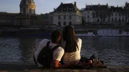 Sepasang kekasih menikmati matahari terbenam di tepi sungai Seine, di Paris (29/3/2021). Sungai ini merupakan salah satu jalur lalu lintas air komersial dan juga menjadi sebuah tujuan wisata, khususnya bagian yang terletak dalam kota Paris. (AP Photo/Thibault Camus)