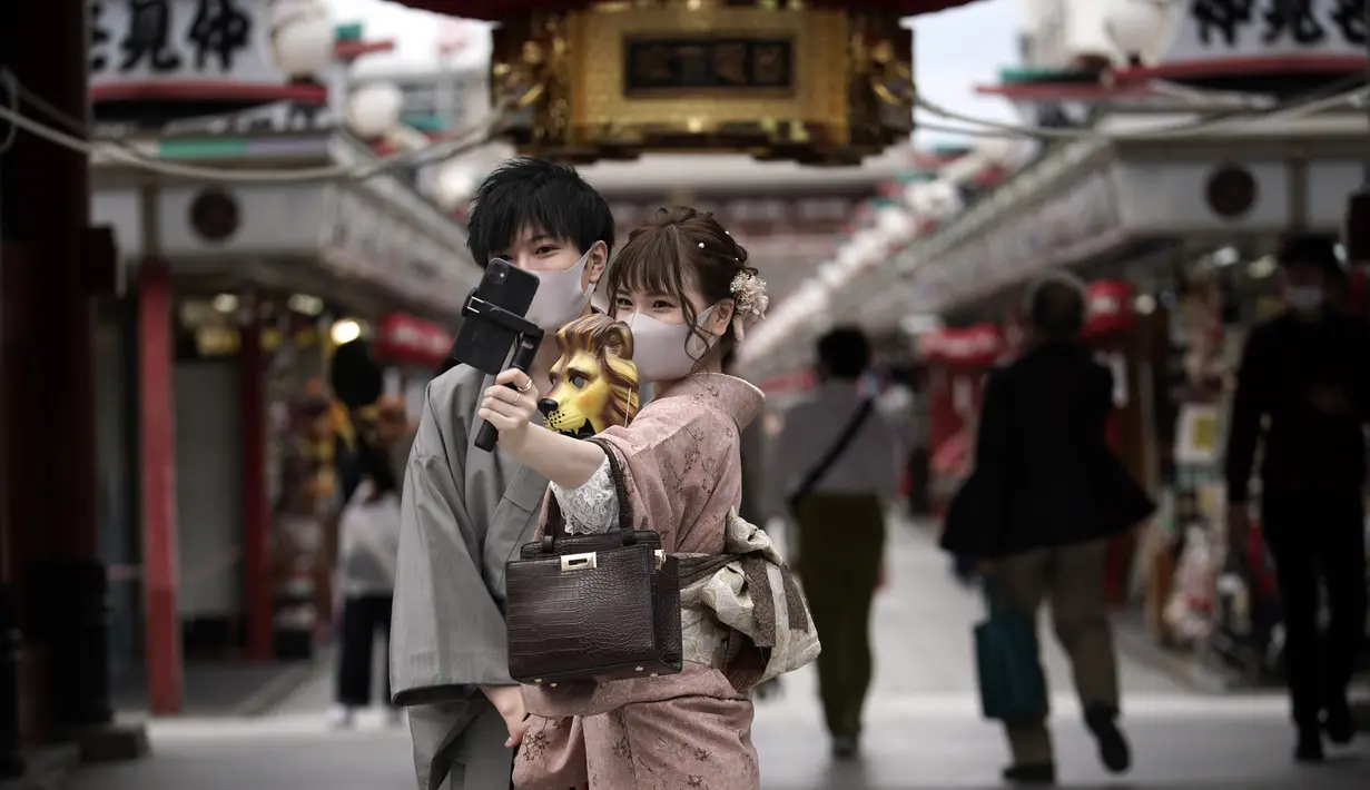 Pengunjung dengan masker pelindung untuk membantu mencegah penyebaran virus corona berfoto selfie di pusat perbelanjaan di distrik Asakusa di Tokyo, Selasa (29/9/2020). kota Jepang mengonfirmasi lebih dari 200 kasus virus corona pada hari Selasa. (AP Photo/Eugene Hoshiko)