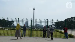 Warga berdiri di depan pagar Monumen Nasional (Monas), Jakarta, Sabtu (15/5/2021). Warga kecewa lantaran tempat wisata tersebut ditutup, padahal mereka datang untuk menikmati libur Idul Fitri 1442 Hijriah. (merdeka.com/Imam Buhori)