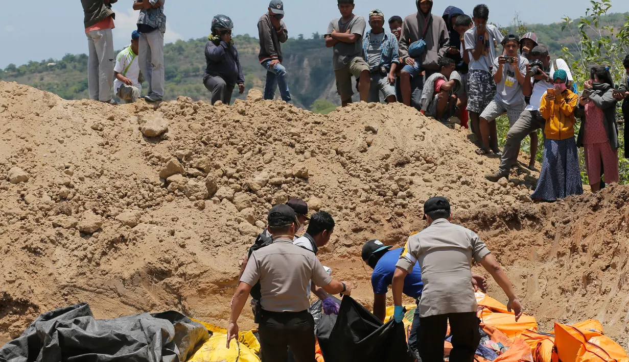 Warga menyaksikan pemakaman massal jenazah korban gempa dan tsunami di Palu, Sulawesi Tengah, Senin (1/10). Gempa dan tsunami yang melanda Palu serta Donggala telah menewaskan ratusan korban jiwa. (AP Photo/Tatan Syuflana)