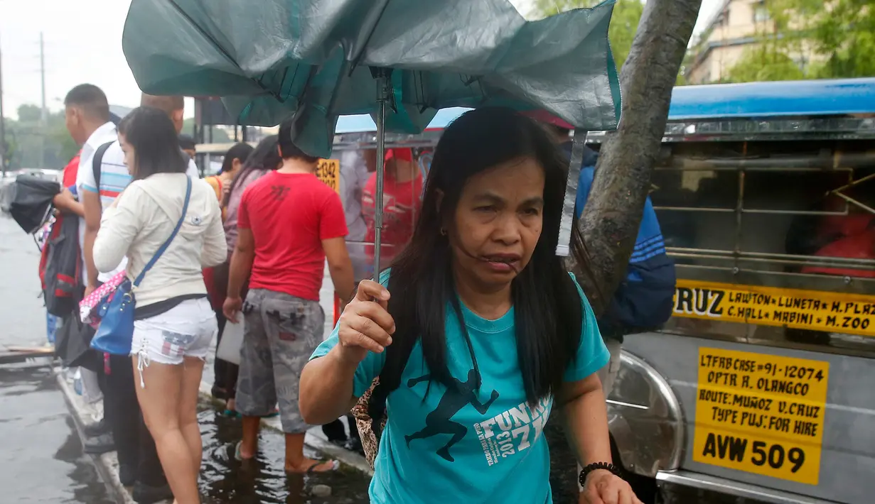 Penduduk sekitar tetap menjalankan aktivitas sehari-hari meskipun hujan lebat membanjiri Manila, Filipina, Kamis (27/7). Diperkirakan akan meningkatnya musim penghujan di wilayah barat daya Manila hingga akhir Juli. (AP/Bullit Marquez)