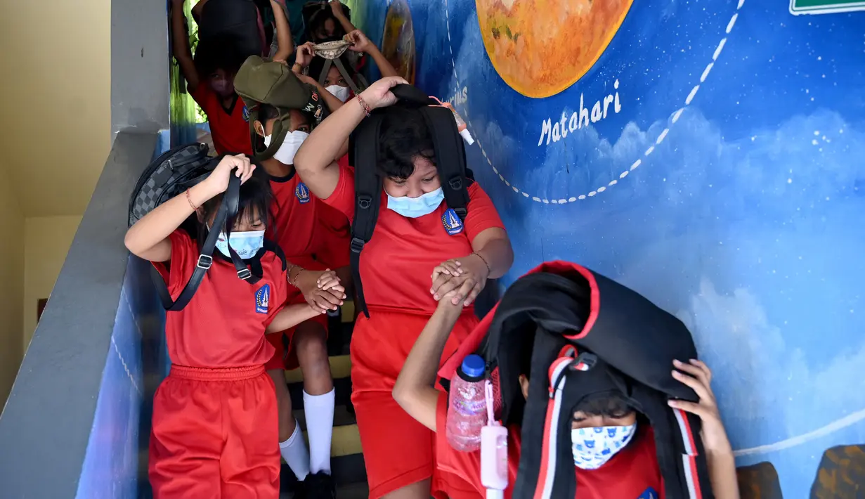 Anak-anak sekolah menggunakan tas mereka untuk melindungi diri saat latihan gempa dan tsunami di Tanjung Benoa, Kabupaten Badung, Bali, 24 Mei 2022. (SONY TUMBELAKA/AFP)