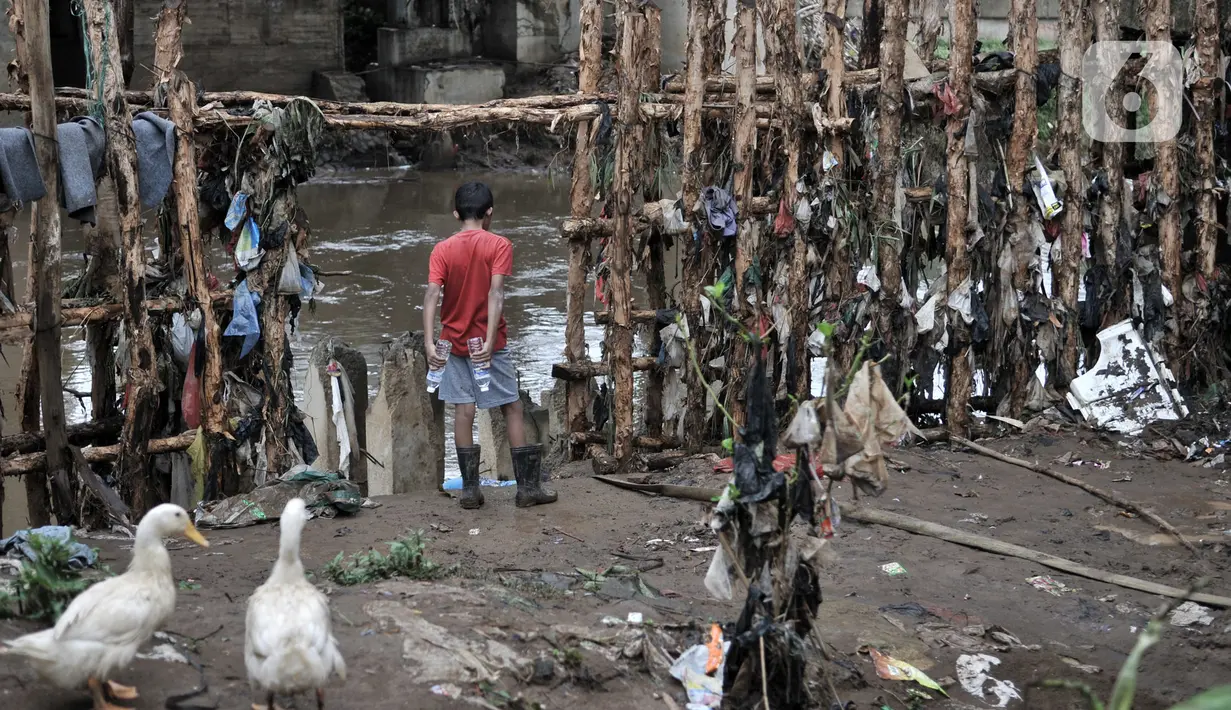 Seorang anak berada di dekat tanggul batang pohon di bantaran Kali Ciliwung, Rawajati, Pancoran, Jakarta, Minggu (5/1/2020). Tanggul dari kayu dolken dan karung pasir yang baru dibangun pada akhir Desember 2019 itu rusak hingga dipenuhi sampah akibat terjangan arus banjir (merdeka.com/Iqbal Nugroho)