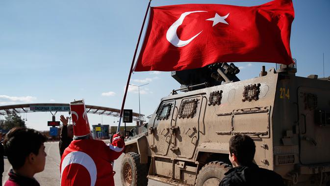 Isikli Tosun Baba (60) melambaikan bendera saat pasukan Turki bergerak melewatinya di Oncupinar, Kilis, Turki, Minggu (28/1). Aksi itu dilakukan untuk mendukung serangan pasukan Turki ke kantung Kurdi di Afrin, Suriah. (AP Photo/Lefteris Pitarakis)