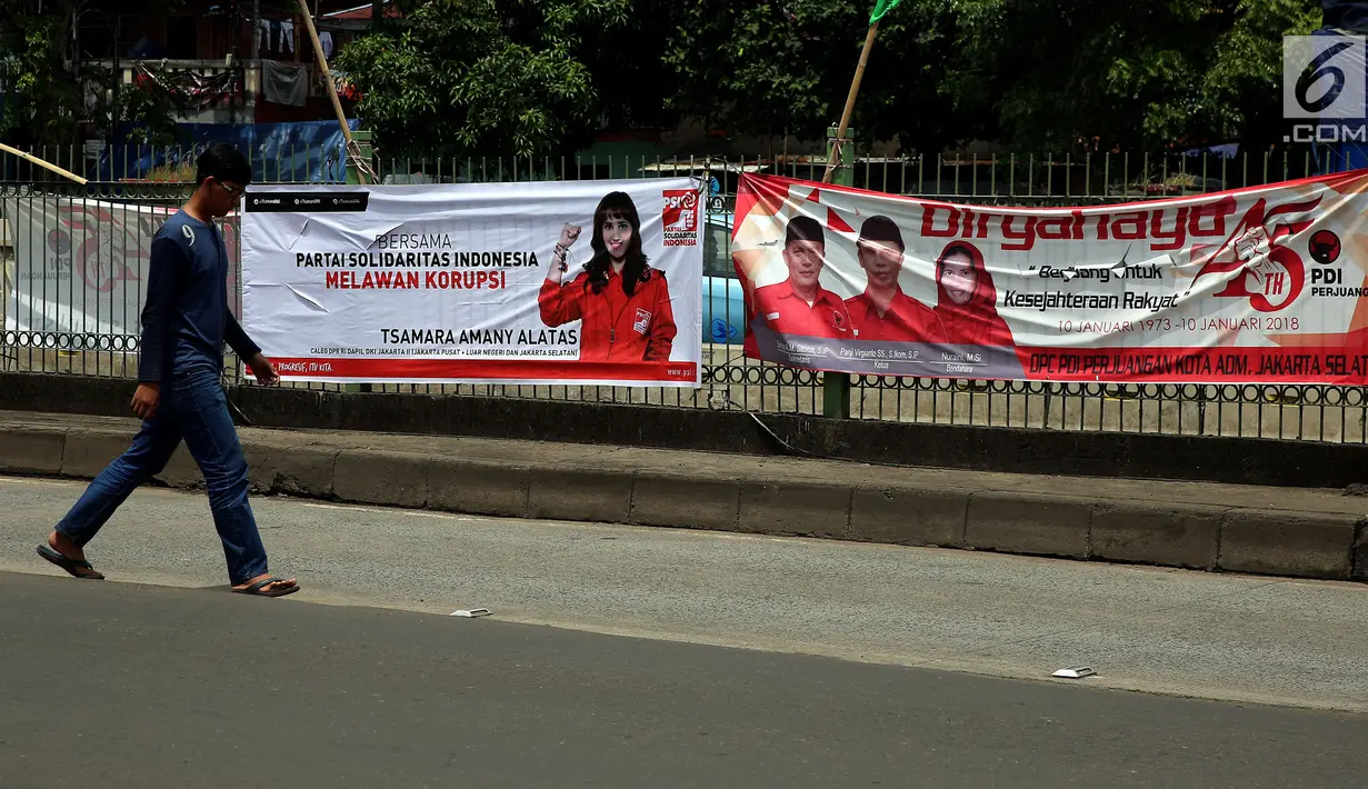 Pejalan kaki berjalan di depan spanduk partai politik yang terpampang di Jalan Sultan Agung, Manggarai, Jakarta, Selasa (16/1). Memasuki 2018, parpol berlomba mengambil hati rakyat dengan berbagai janji terpampang di spanduknya. (Liputan6.com/JohanTallo)