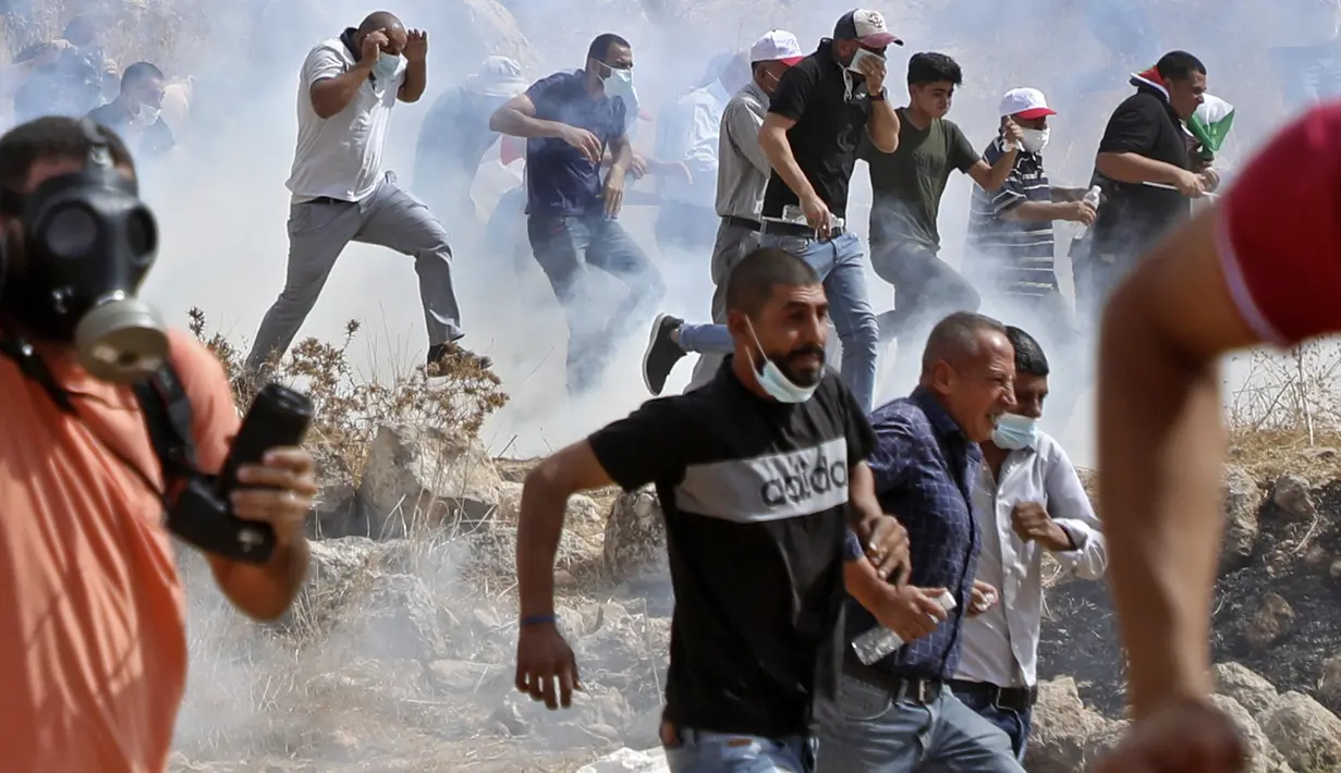 Pengunjuk rasa Palestina menghindari gas air mata yang ditembakkan tentara Israel saat memprotes pencaplokan tanah untuk perluasan permukiman Yahudi di dekat desa Beit Dajan, timur Nablus, Palestina (9/10/2020). (AFP/Jaafar Ashtiyeh)
