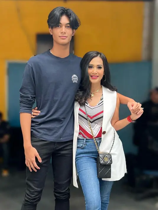 Dirangkul sang anak yang memiliki tubuh sangat tinggi, Diah Permatasari tampil stylish di foto ini. Ia mengenakan atasan tanpa lengan bermotif garis, ditumpuk dengan vest putih, dan dipadu celana jeans. Sedangkan sang anak kembali tampil kasual dengan atasan lengan panjang tanpa kerah berwarna biru dan celana jeans hitam. [Foto: Instagram/dps_diahpermatasari]