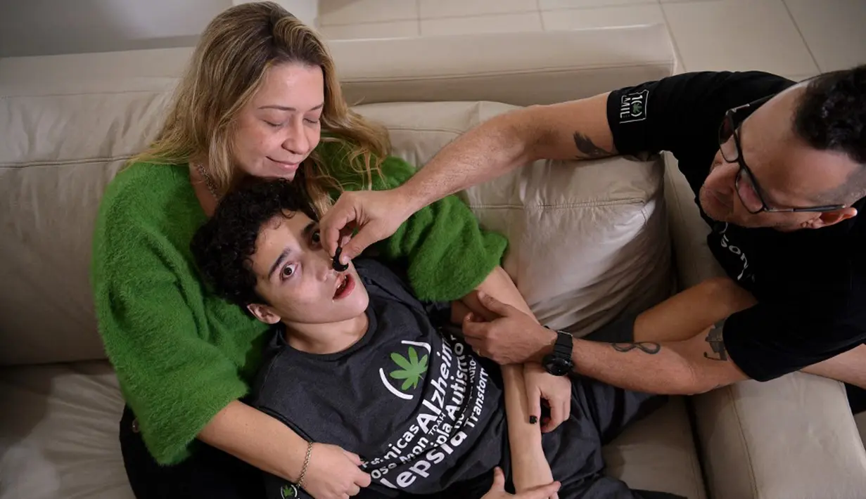 Gabriel Guerra (tengah) digendong ibunya Vanessa Opitz sedangkan ayahnya Ricardo Guerra memberinya ganja obat di Rio de Janeiro, Brasil, 20 September 2021. Ricardo memberi ganja obat kepada Gabriel dalam bentuk tetesan untuk membantu anaknya dari autisme berat dan cerebral palsy. (CARL DE SOUZA/AFP)