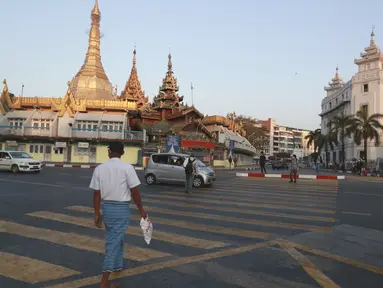 Orang-orang menyeberang jalan dekat Pagoda Sule di Yangon, Myanmar pada Senin (1/2/2021). Militer Myanmar resmi merebut kekuasaan pemerintah usai menahan Kanselir Aung San Suu Kyi dan Presiden Myint pada Senin pagi (1/2). (AP Photo/Thein Zaw)