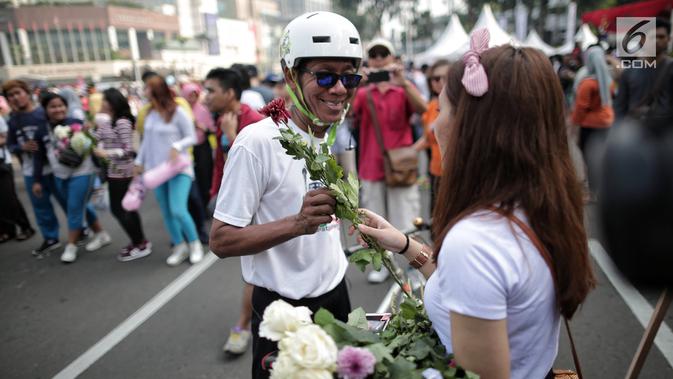 Anggota TKN Milenial Jokowi-Ma'ruf membagikan bunga kepada pengunjung car free day dalam kegiatan tabur bunga di Bundaran HI, Jakarta, Minggu (28/4/2019). Mereka mengajak masyarakat untuk ikut mengungkapkan duka atas meninggalnya 272 petugas KPPS dalam Pemilu 2019. (Liputan6.com/Faizal Fanani)