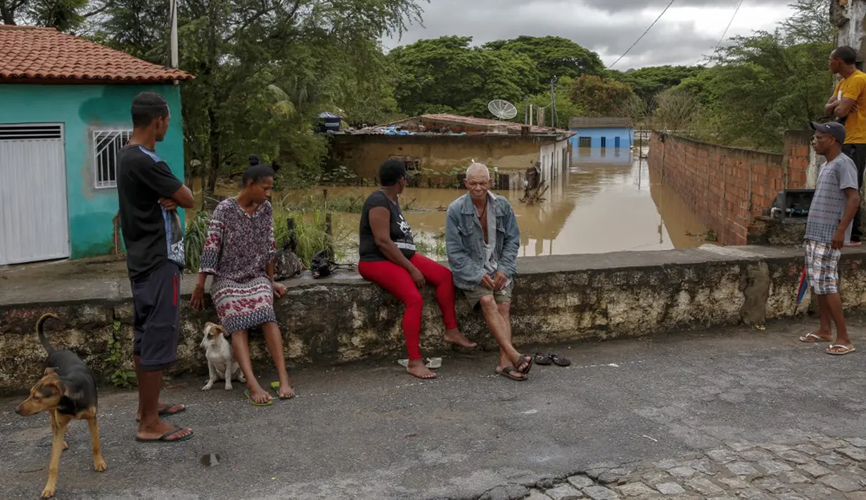 Orang-orang tetap di tempat yang kering saat banjir akibat hujan lebat di Itapetinga, Negara Bagian Bahia, Brasil, 26 Desember 2021. Banjir membuat 35.000 orang terpaksa mengungsi. (Manuella LUANA/AFP)